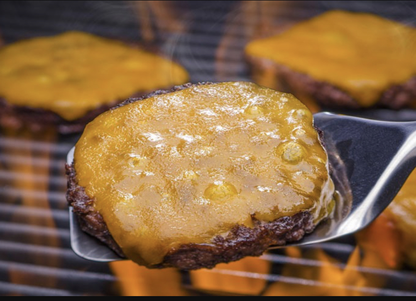 three venison burger patties on a grill covered with yellow cheese.