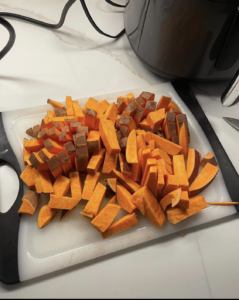 Orange sweet potato with brown skin cut into small rectangles sitting on a plastic cutting board on a white granite counter