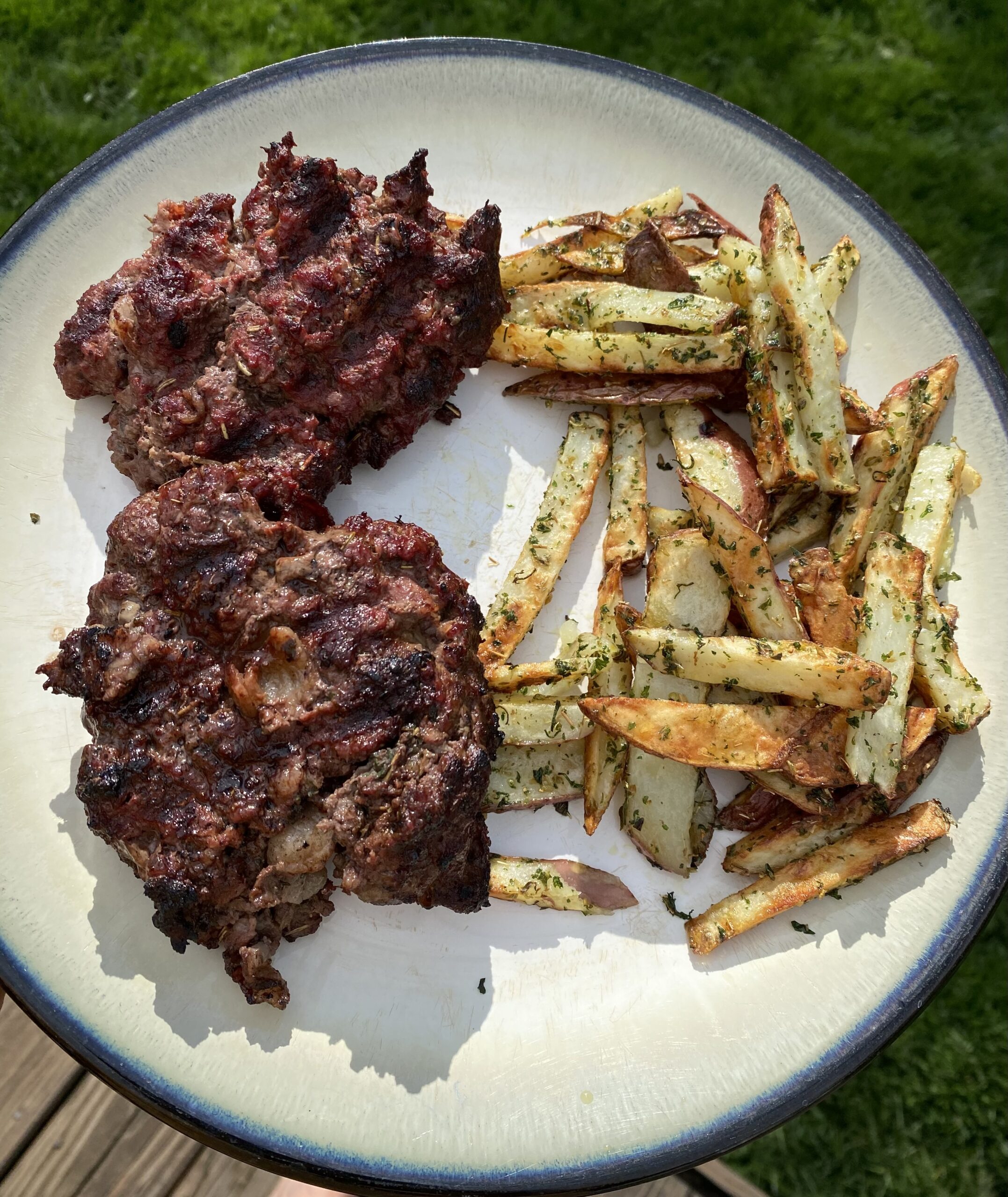 White plate with grass in the background. Plate is full of burgers and fresh potato french fries