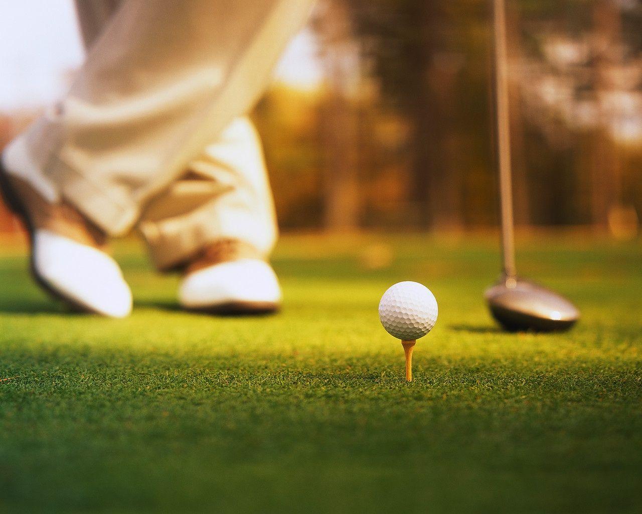 Golfer stands next to a golf club and a ball resting on a golf tee.